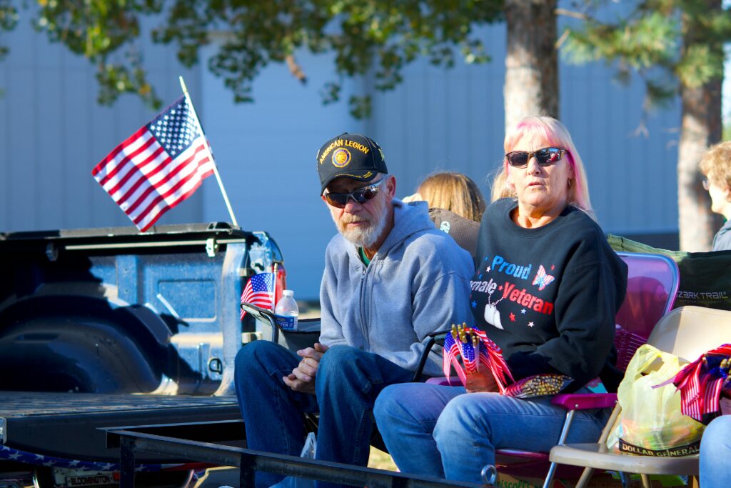 pexels-photo-34148638-34148638 Senior veteran couple in a parade setting with American flags, showcasing patriotism and community spirit.